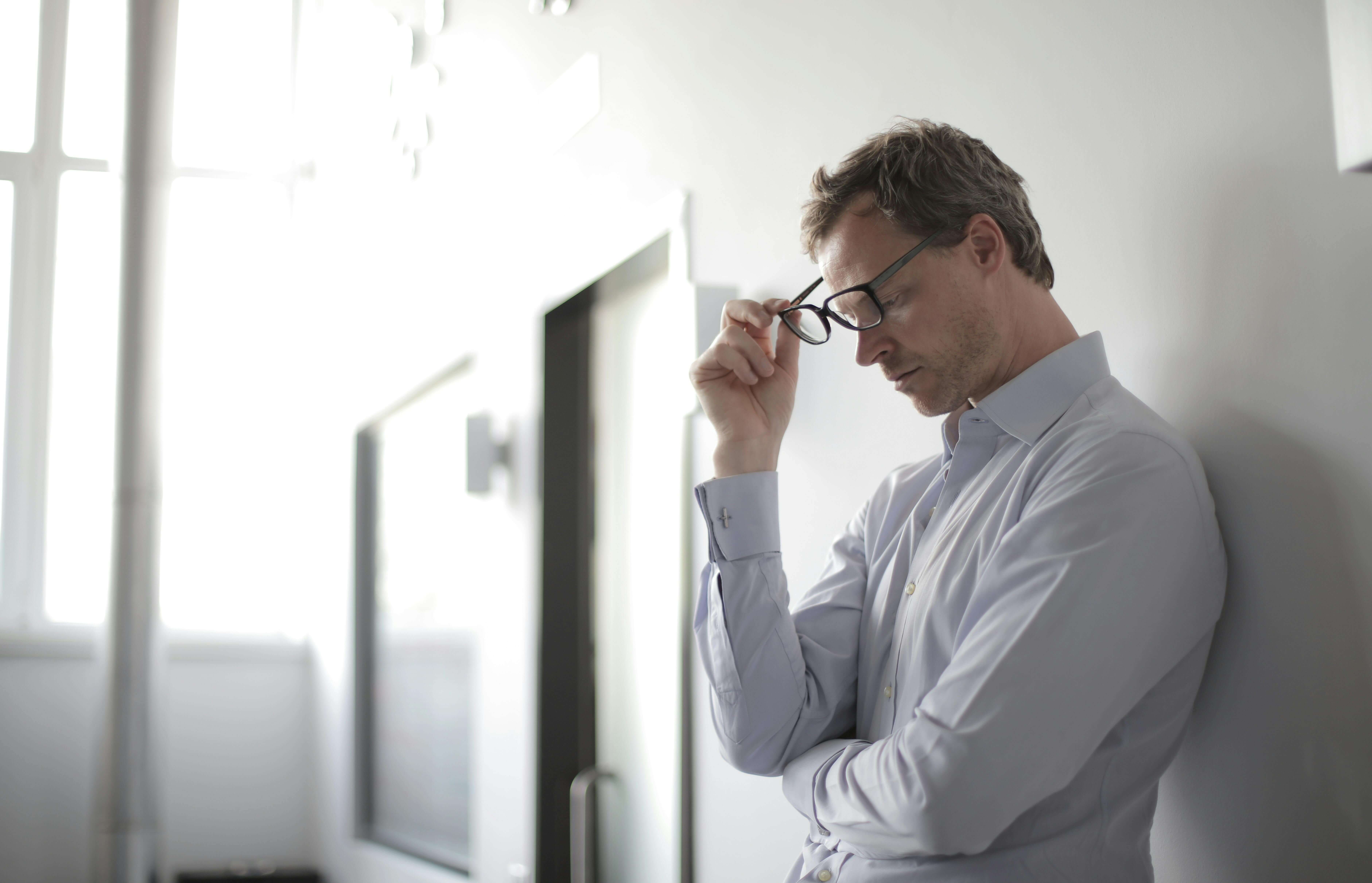 stressed man with his head in his hands holding his glasses